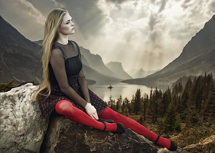 woman in black dress sitting on rock under white skies thumbnail