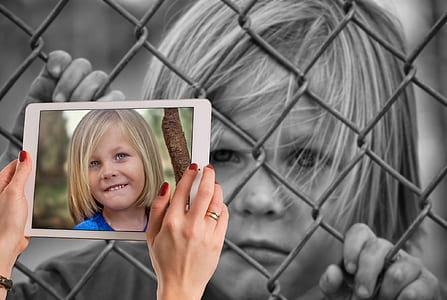grayscale photograph of boy holding on chain link fence thumbnail