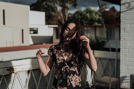woman wearing black and pink floral cap-sleeved surplice-neck dress standing near white handrail thumbnail