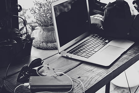 grayscale photo of MacBook air beside sunglasses and power bank on table thumbnail