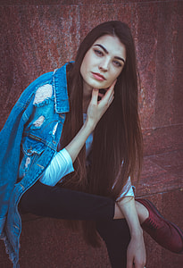 woman with blue denim distressed jacket sitting near red wall thumbnail