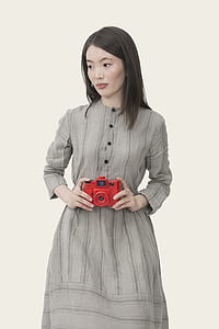 woman in gray dress holding red camera thumbnail