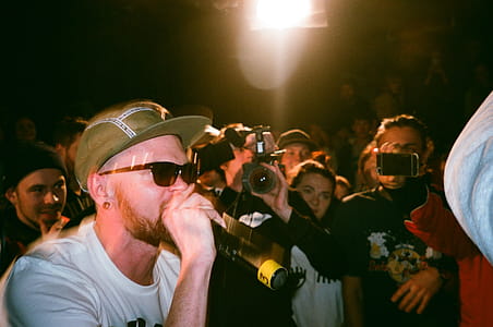 Man Speaking on Microphone Surrounded by People Taking Photo thumbnail