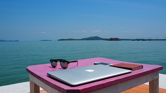 silver MacBook beside black sunglasses and smartphone on pink wooden table thumbnail