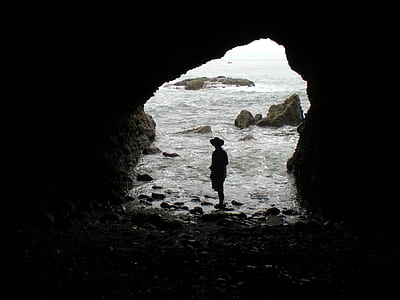 person standing inside cave near body of water thumbnail
