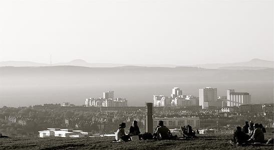 grayscale photography of people sitting on ground while looking at city thumbnail