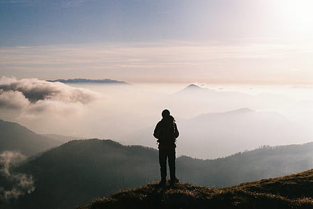 silhouette photo of man standing on mountain looking at clouds thumbnail