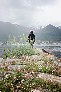 person in black jacket standing on rock formation looking at sea during daytime thumbnail