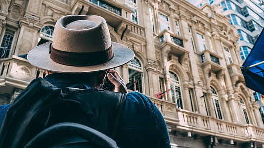 Man in Beige Hat Taking Picture on Beqige Conrete Architectural Building thumbnail