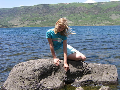 woman sitting on brown sock beside body of water during daytime thumbnail