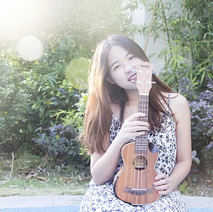 woman holding ukulele standing near plant thumbnail