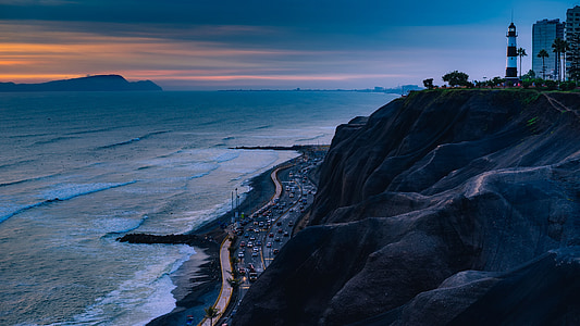 vehicles on road beside cliff near body of water thumbnail