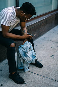 man sitting on concrete holding jacket and using cellphone thumbnail