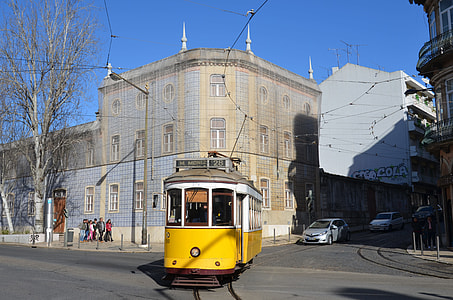 yellow city tram in front of gray building thumbnail