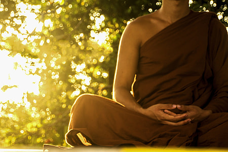 Monk wearing brown robe meditating during golden hour thumbnail
