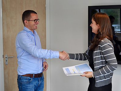 man in blue dress shirt shaking hands with woman in white and grey striped zip-up jacket thumbnail