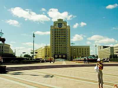 Woman Standing on Ground Overlooking White Concrete Building thumbnail