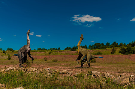two dinosaurs on green grass field under blue and white cloudy sky thumbnail