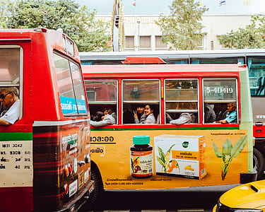 two smiling people inside bus in street with two buses and cab near building with flag on top during daytime thumbnail