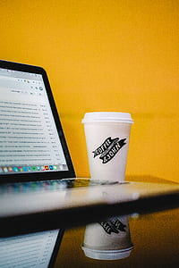 white coffee cup near laptop computer on table thumbnail