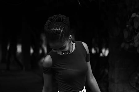 grayscale photo of woman standing beside trees thumbnail