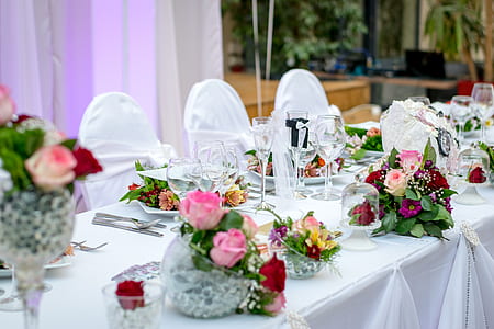 three flower arrangements on top of white table near drinking glasses and plates thumbnail