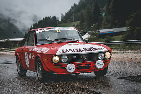 Lancia-Marlboro race car on road near tree covered hill thumbnail