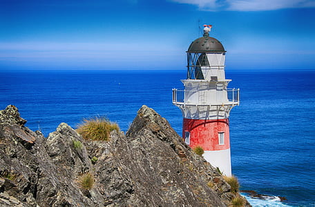 white and red lighthouse near grey rock formation and sea during daytime thumbnail