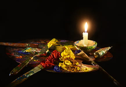 assorted paint brush on palette near lighted candle thumbnail