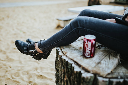Beautiful blonde woman relaxing with a can of coke on a tree stump by the beach thumbnail