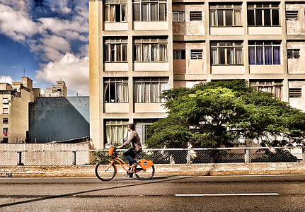 man riding orange cruiser bike near beige building thumbnail