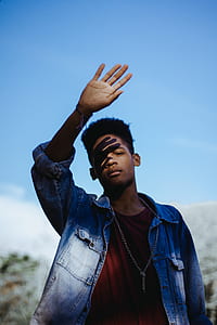 man lifting up his hand covering his eye from the sun light standing under blue daytime sky thumbnail