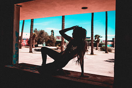 woman holding her head while posing on window at daytime thumbnail