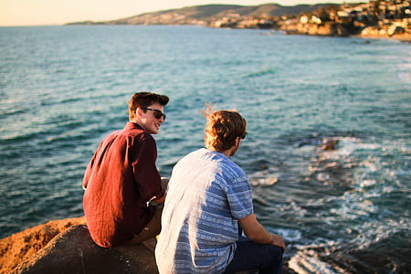 two men sitting on rock by the sea at daytime thumbnail