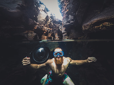 topless man diving underwater while holding camera behind cave at daytime thumbnail