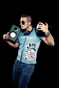 Black Haired Man Wearing Blue Printed Shirt Holding Speakers thumbnail