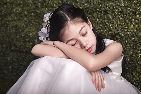 girl sleeping on her crossed arms while sitting next to green wall thumbnail