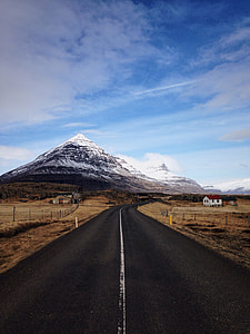 clear road in between brown field near mountain under white clouds and blue sky thumbnail