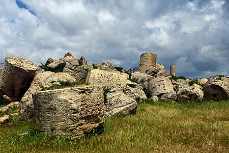 piles of brown boulders on green grass under cloudy sky thumbnail
