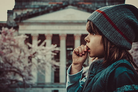 selective focus photo of child eating her finger standing beside wall during daytime thumbnail