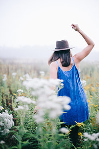 woman walking along flower field while rising her right hand thumbnail