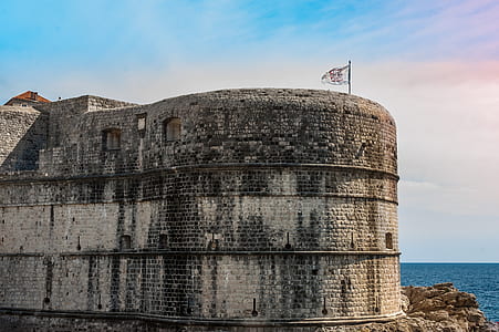 gray concrete brick building with flag near sea at daytime thumbnail