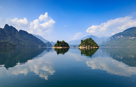 two islands near mountains and glassy water at daytime thumbnail