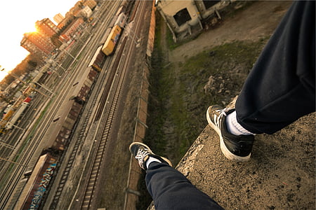 person wearing black-and-white adidas sneakers sitting on rock looking on trains and railways thumbnail