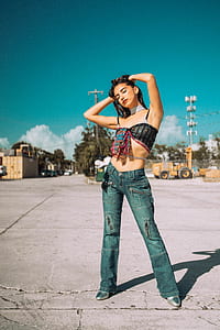woman wearing black spaghetti strap sleeveless shirt and blue pants holding her head while taking photo thumbnail
