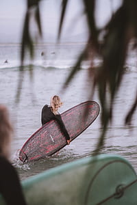 person carrying red and black surfboard on body of water thumbnail