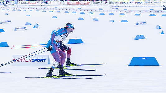 two men riding snow ski blades on snow surface with obstacles during daytime thumbnail