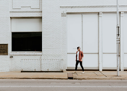 man wearing brown jacket walking near white steel gate thumbnail