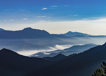 aerial photo of mountains with green trees surrounded by clouds under blue sky at daytime thumbnail