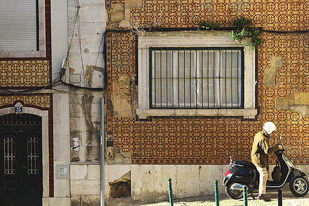 man riding on motor scooter beside house thumbnail